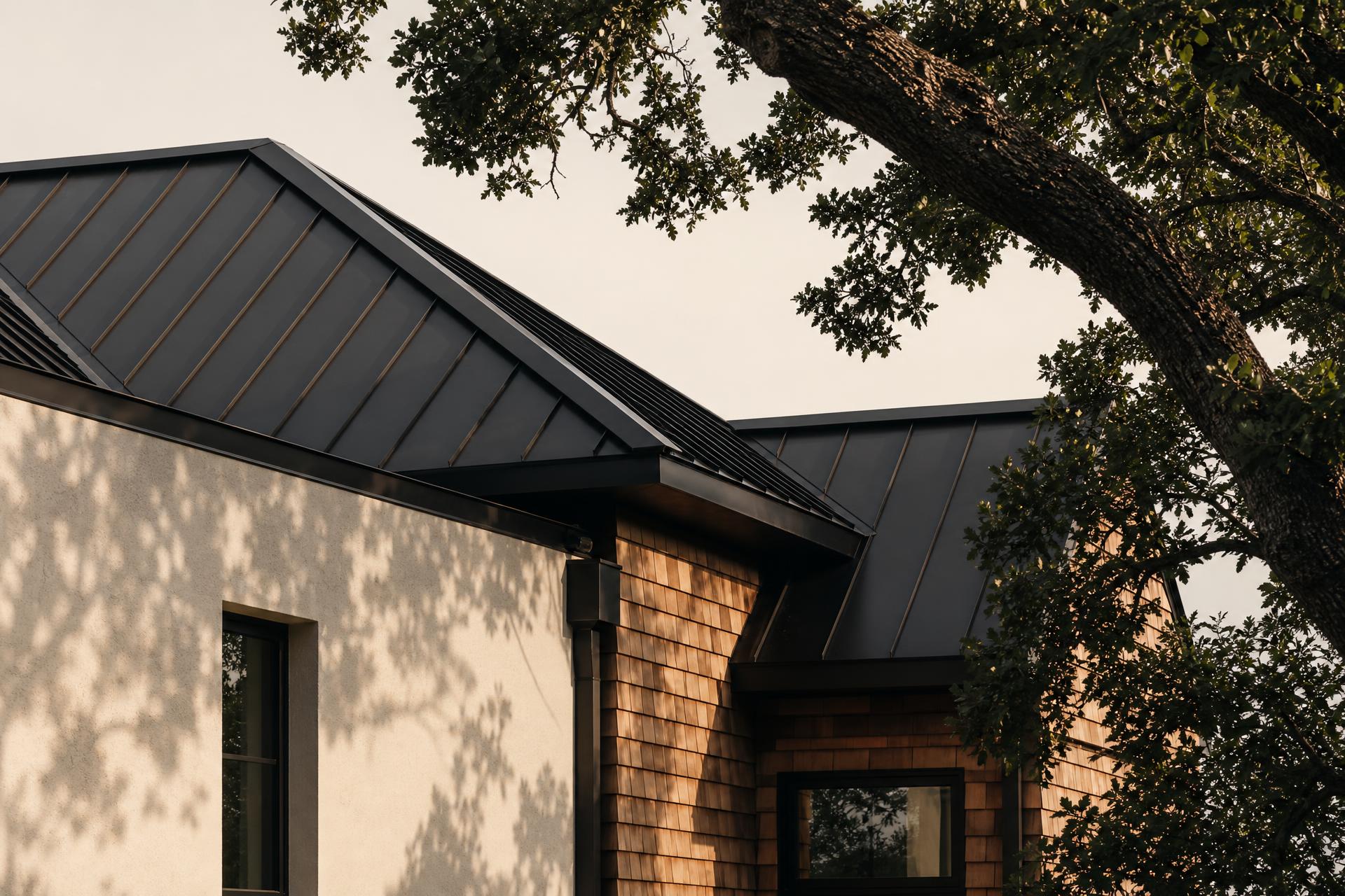 Architectural detail of a modern home with black metal standing-seam roof, cedar shake, and cream stucco under live oak canopy